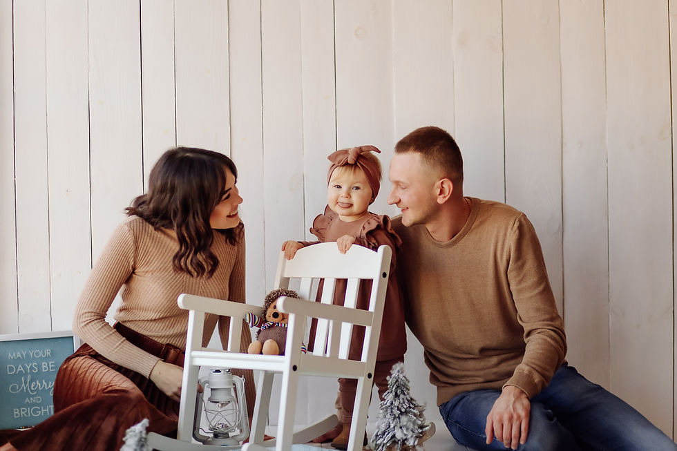 Man and woman smile at a child standing behind a chair